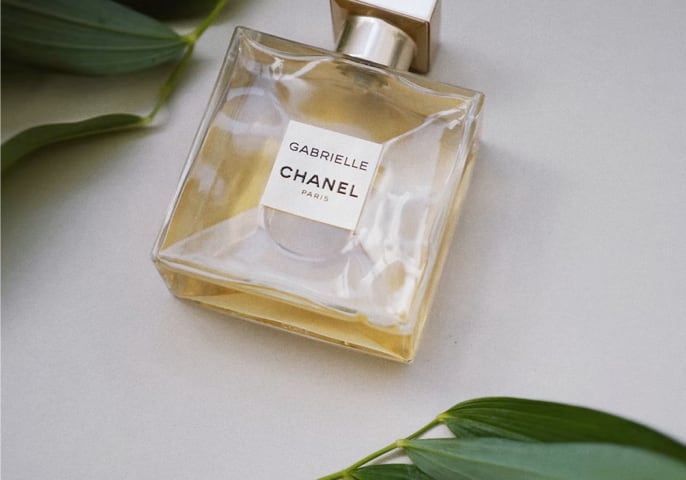 Gabrielle Chanel square perfume bottle on table with leaves beside it